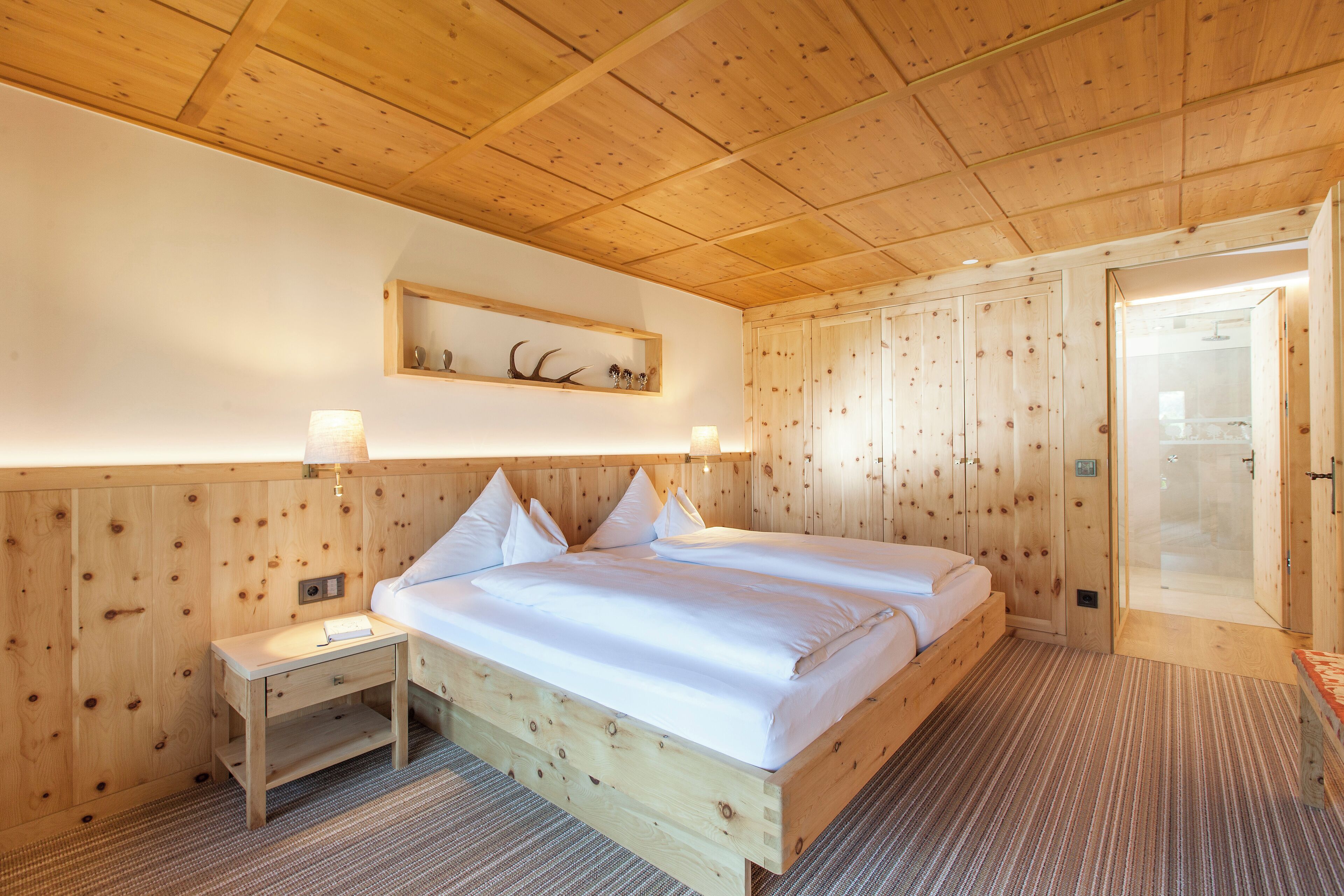 A wooden-paneled room with a bed, bedside tables, and a shower area.