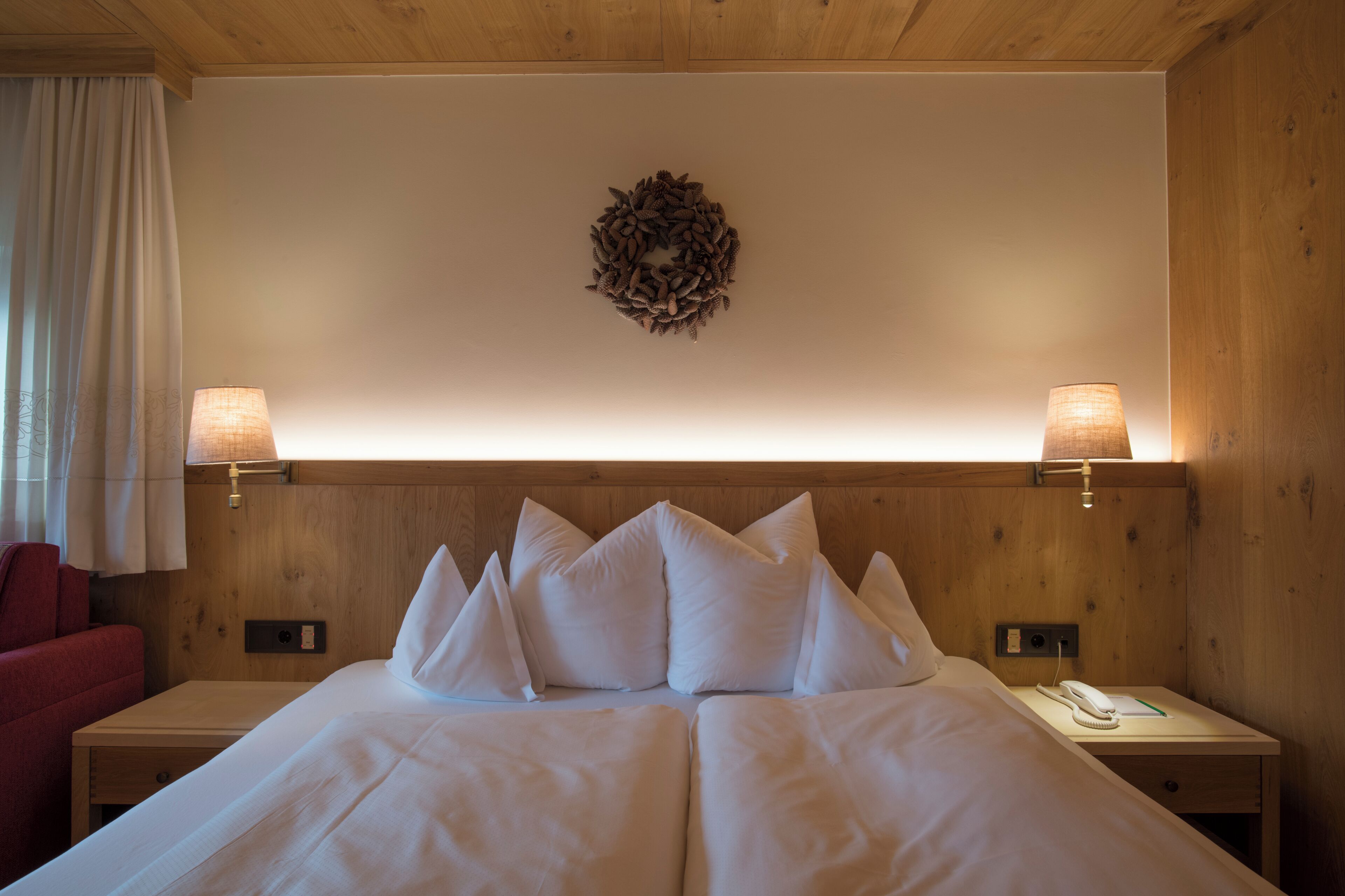 Una habitación de hotel con una cama, dos mesitas de noche, un teléfono, una lámpara y una silla roja.