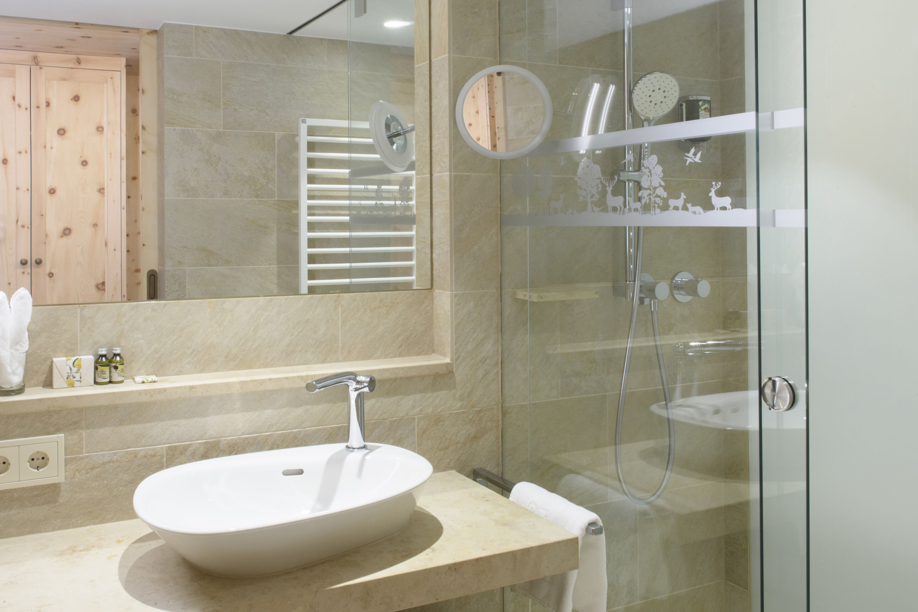 A modern bathroom with a large oval sink, a glass shower enclosure, and a wooden door.
