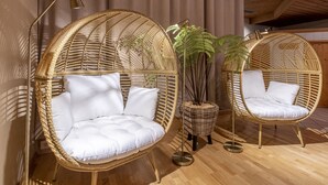Two wicker chairs with white cushions, a potted plant, and a floor lamp in a room with wooden flooring and curtains. - Montafoner Hof (Tschagguns)