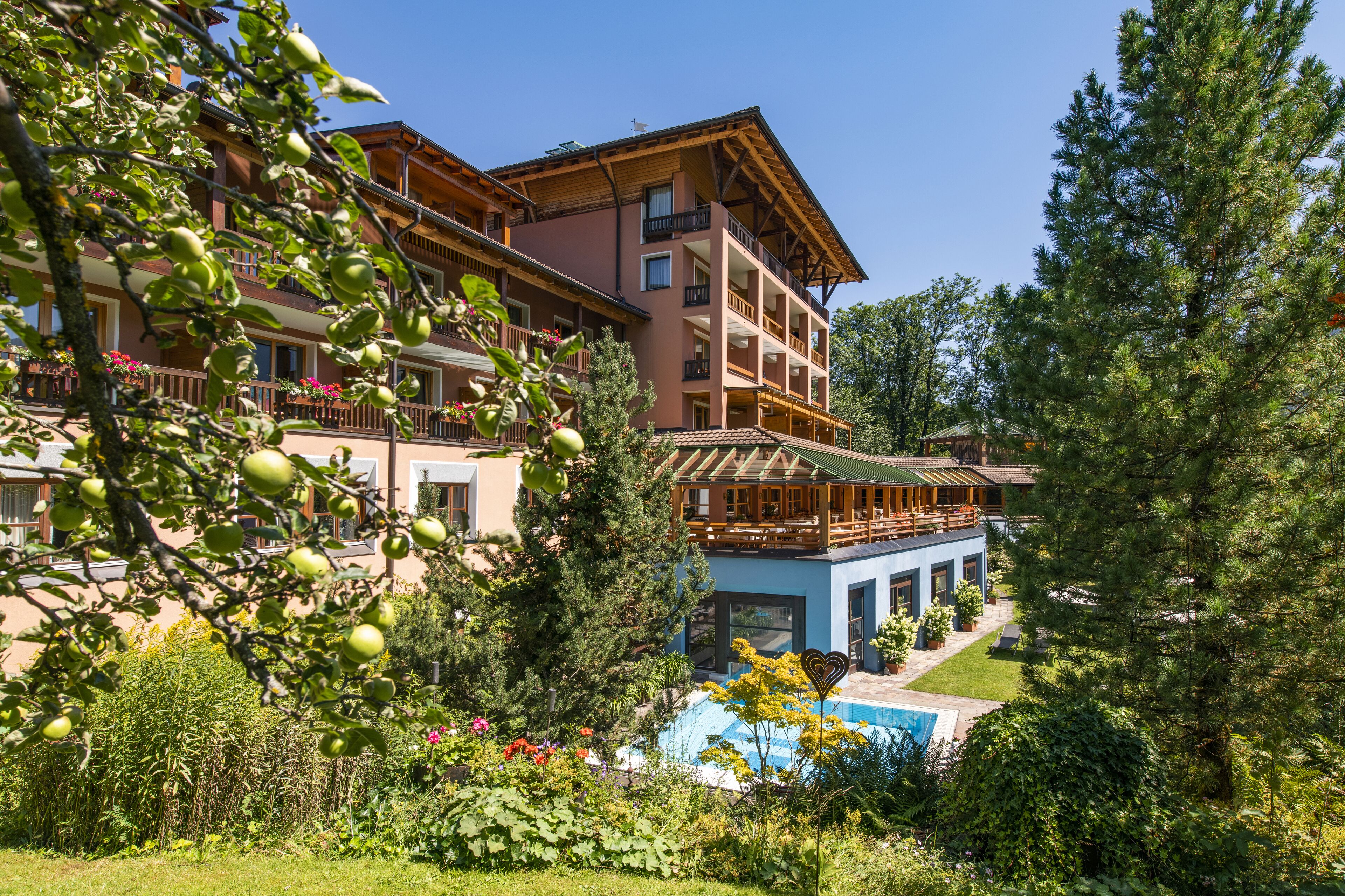 Un hotel de varios pisos con balcones, piscina y abundante vegetación.