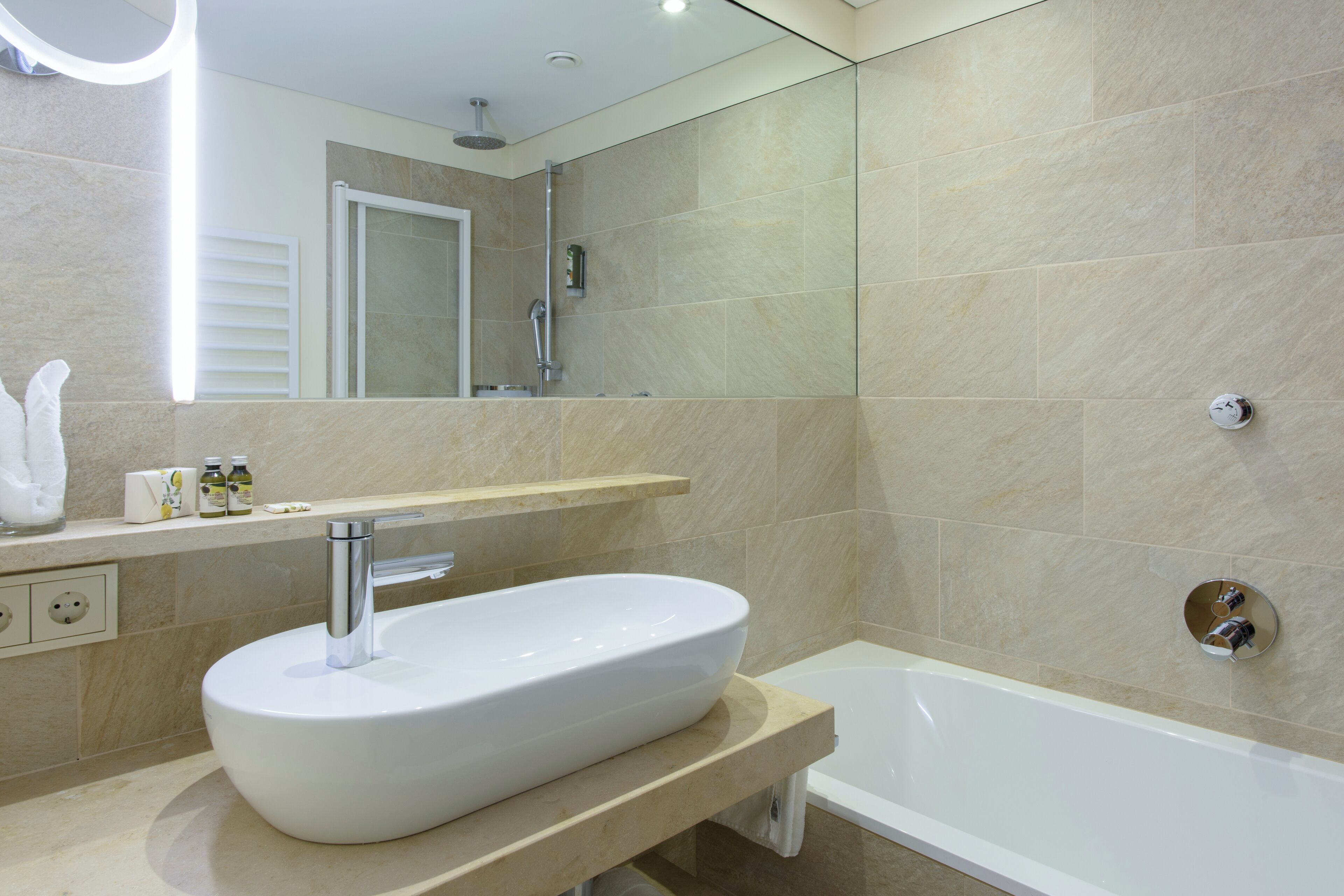 Ein modernes Badezimmer mit einer großen, weißen Badewanne, einem runden Waschbecken und einem Spiegel darüber.