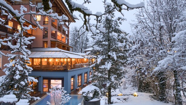 A multi-story hotel with a pool area, surrounded by snow-covered trees and a clear sky. - Montafoner Hof (Tschagguns)