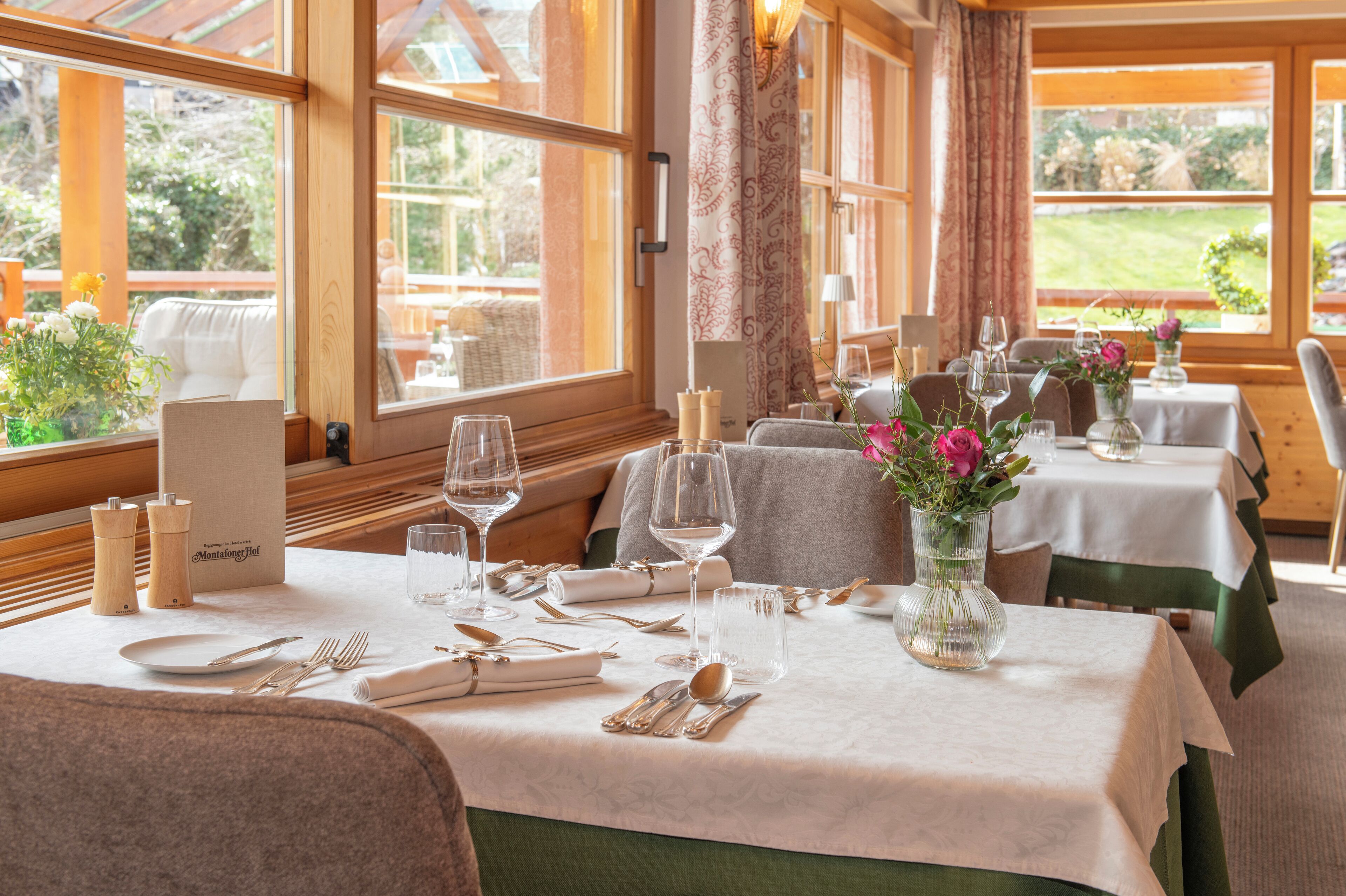 A dining area with tables set for a meal, featuring white tablecloths, glassware, and floral centerpieces.