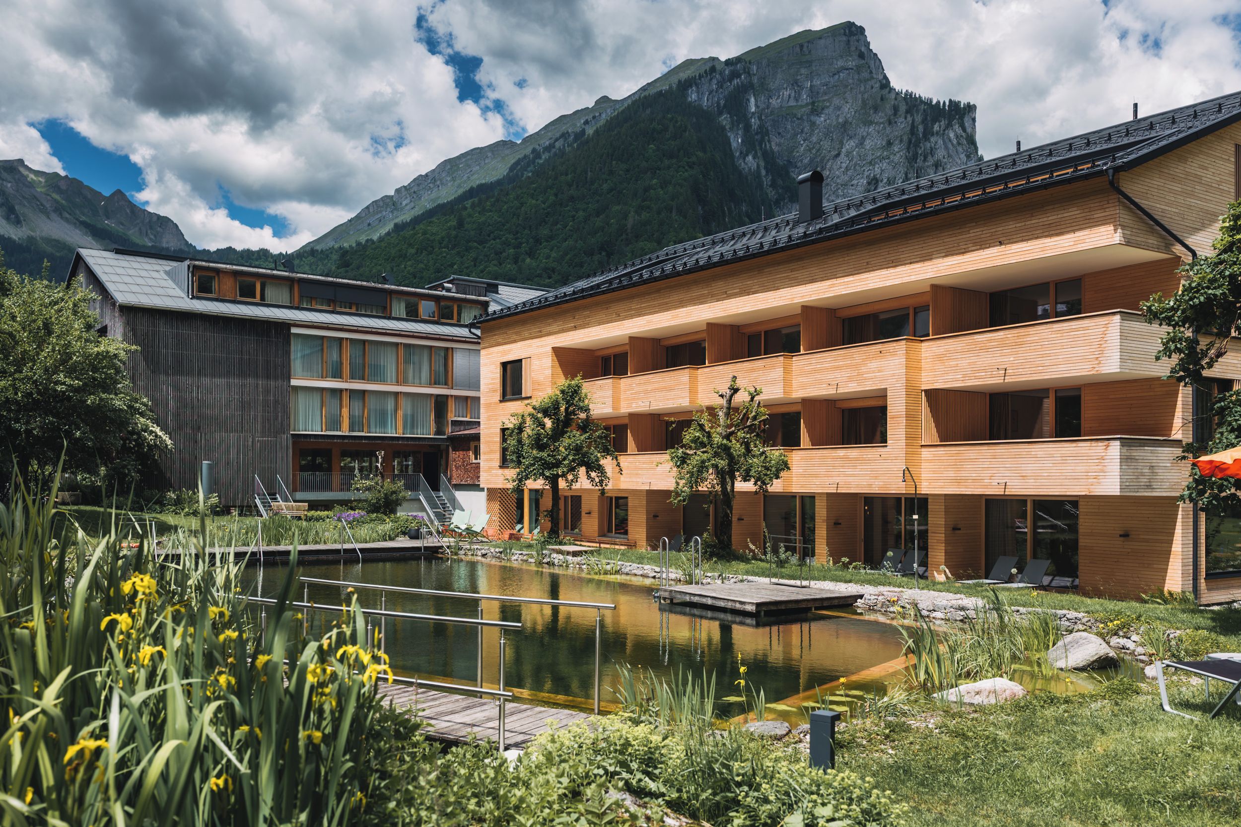 A modern building with a wooden facade, a small pond, and a mountain backdrop.