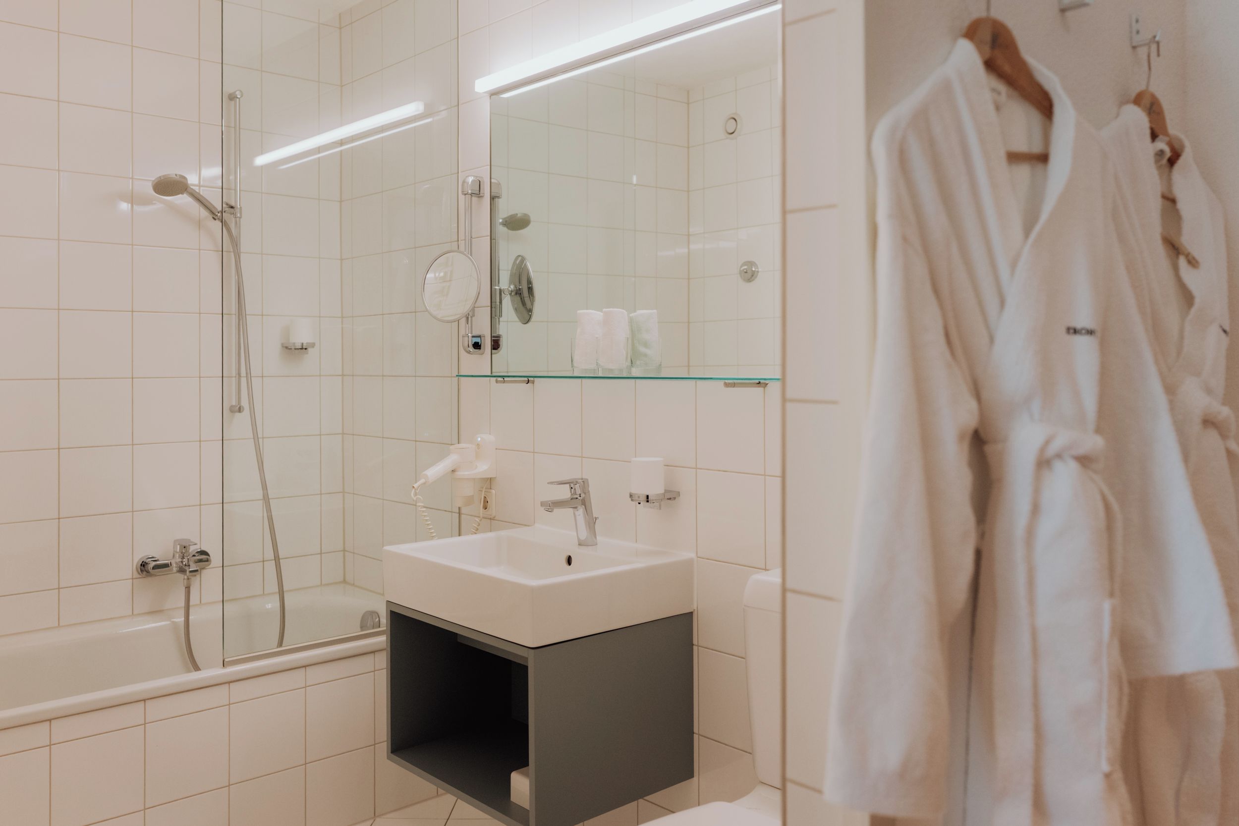 A modern bathroom with a glass shower enclosure, a vanity with a mirror, and a hanging robe.