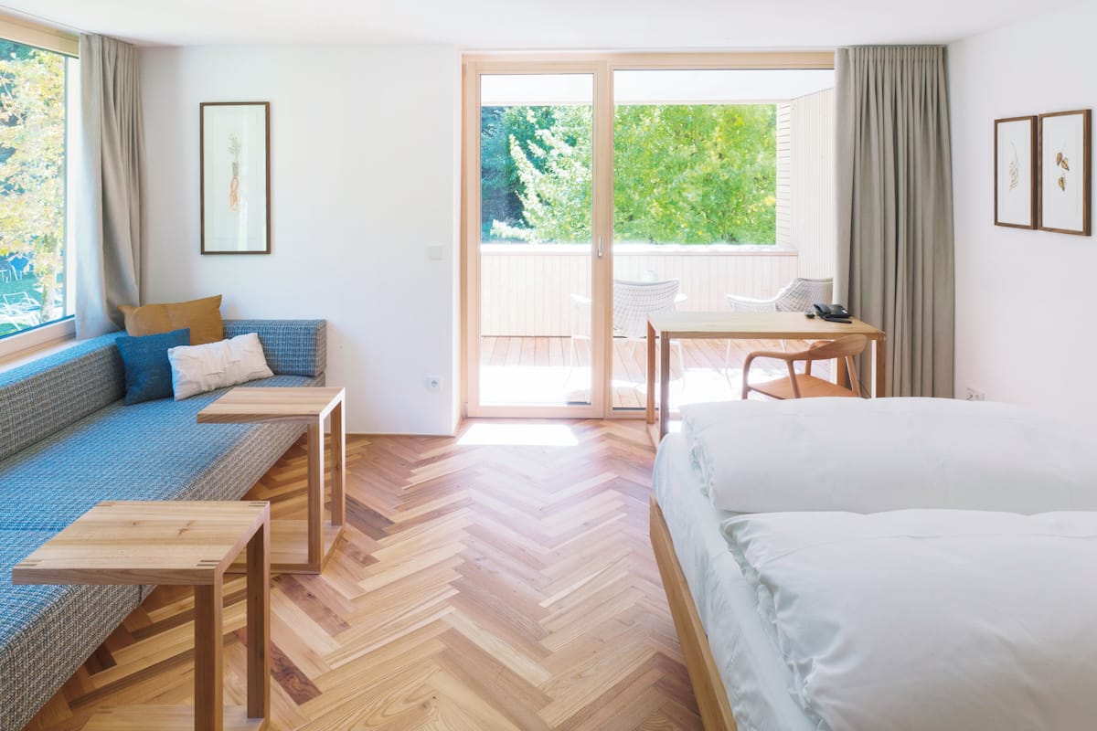 A modern room with a sofa, a bed, a table, and a balcony with a view of trees.