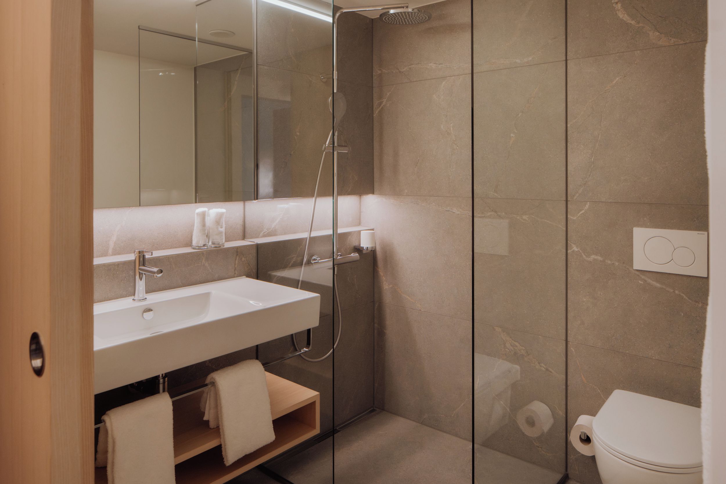 A modern bathroom with a glass-enclosed shower, a white sink, and a toilet.
