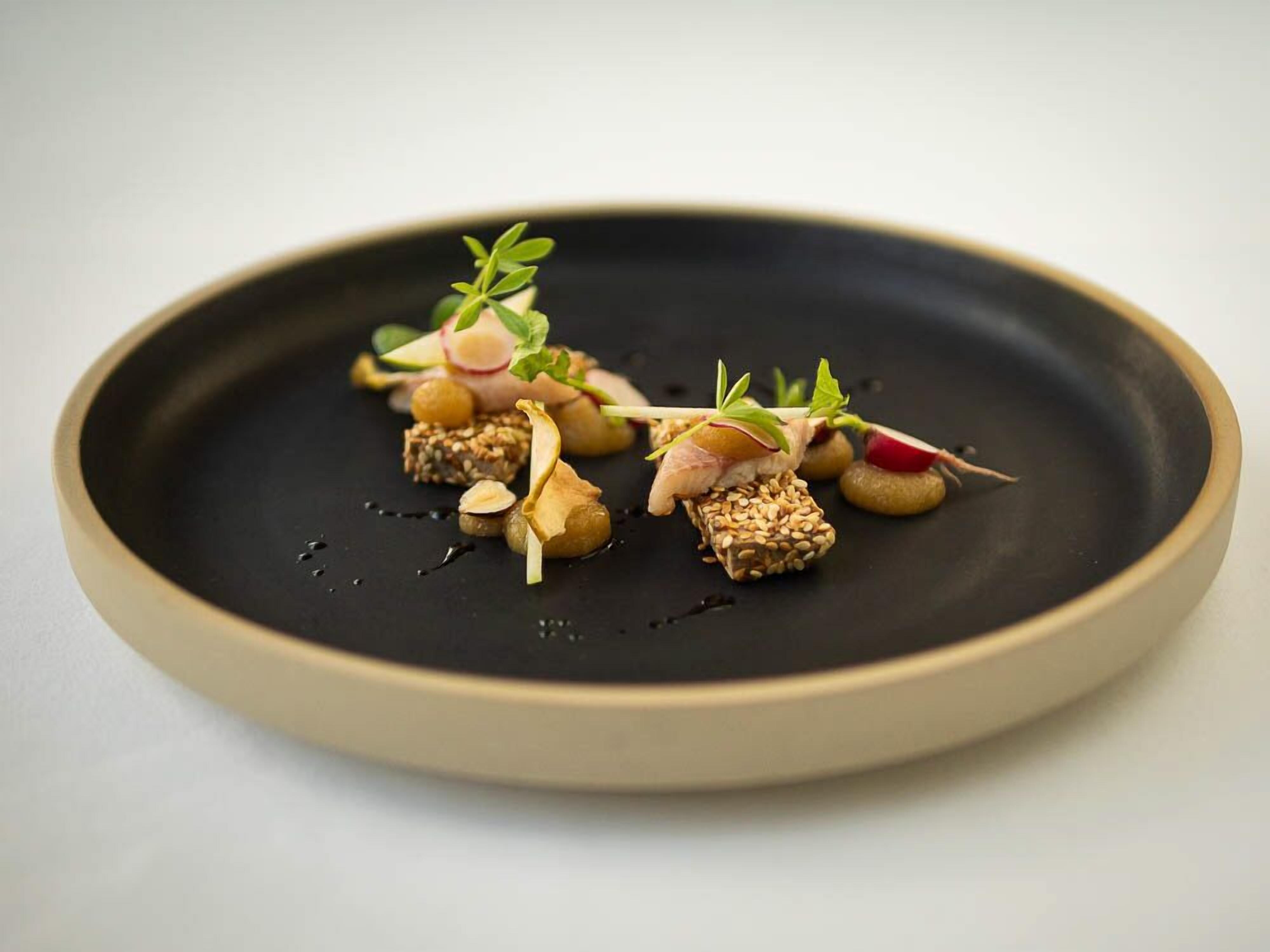 A black plate with a variety of food items, including sushi, nuts, and vegetables.