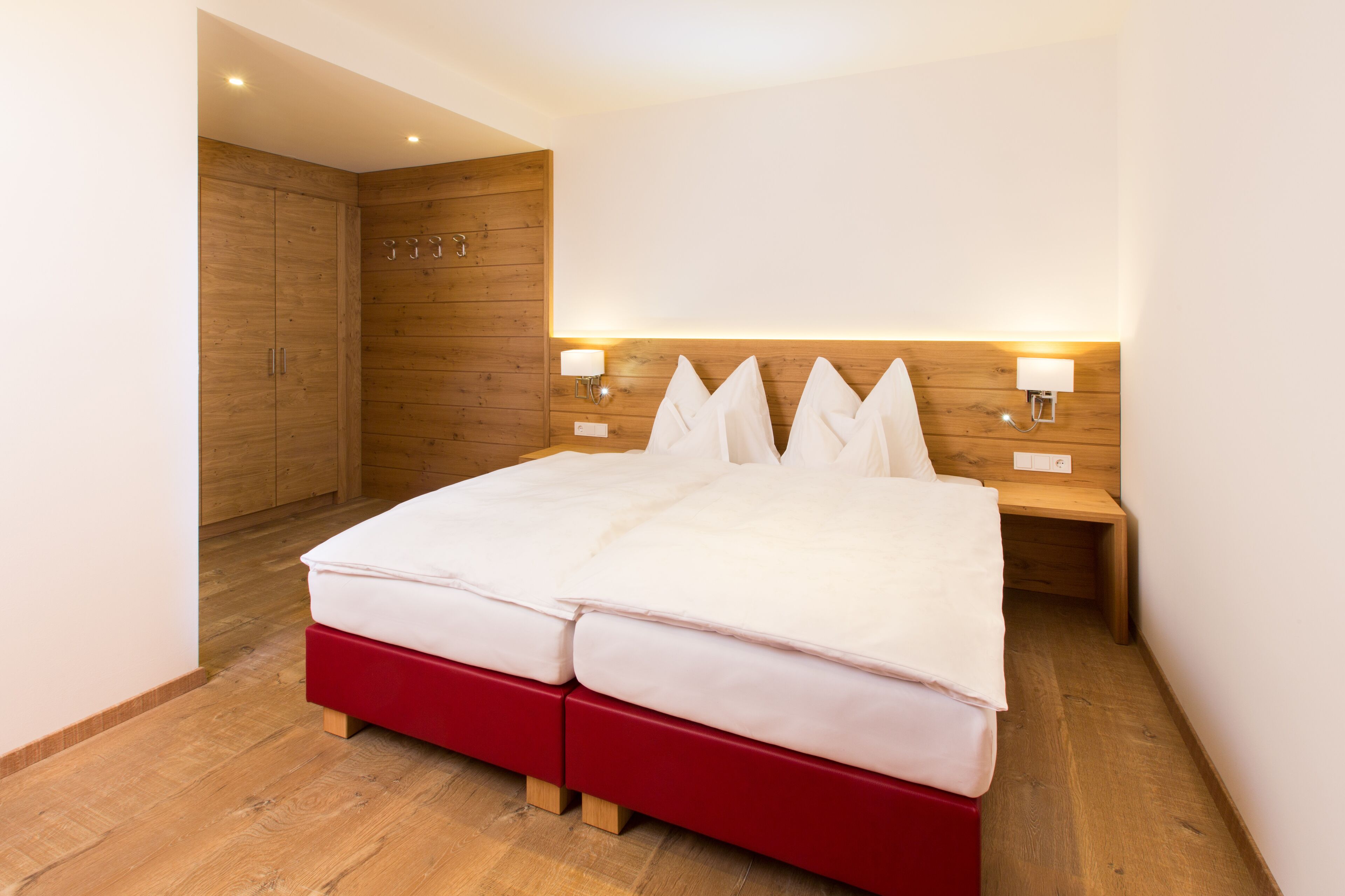 A modern hotel room with a large bed, wooden wardrobe, and bedside lamps.