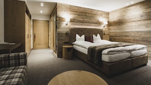 Un dormitorio moderno con cabecera de madera, cama con ropa de cama blanca, una mesa redonda de madera y un sofá a cuadros.