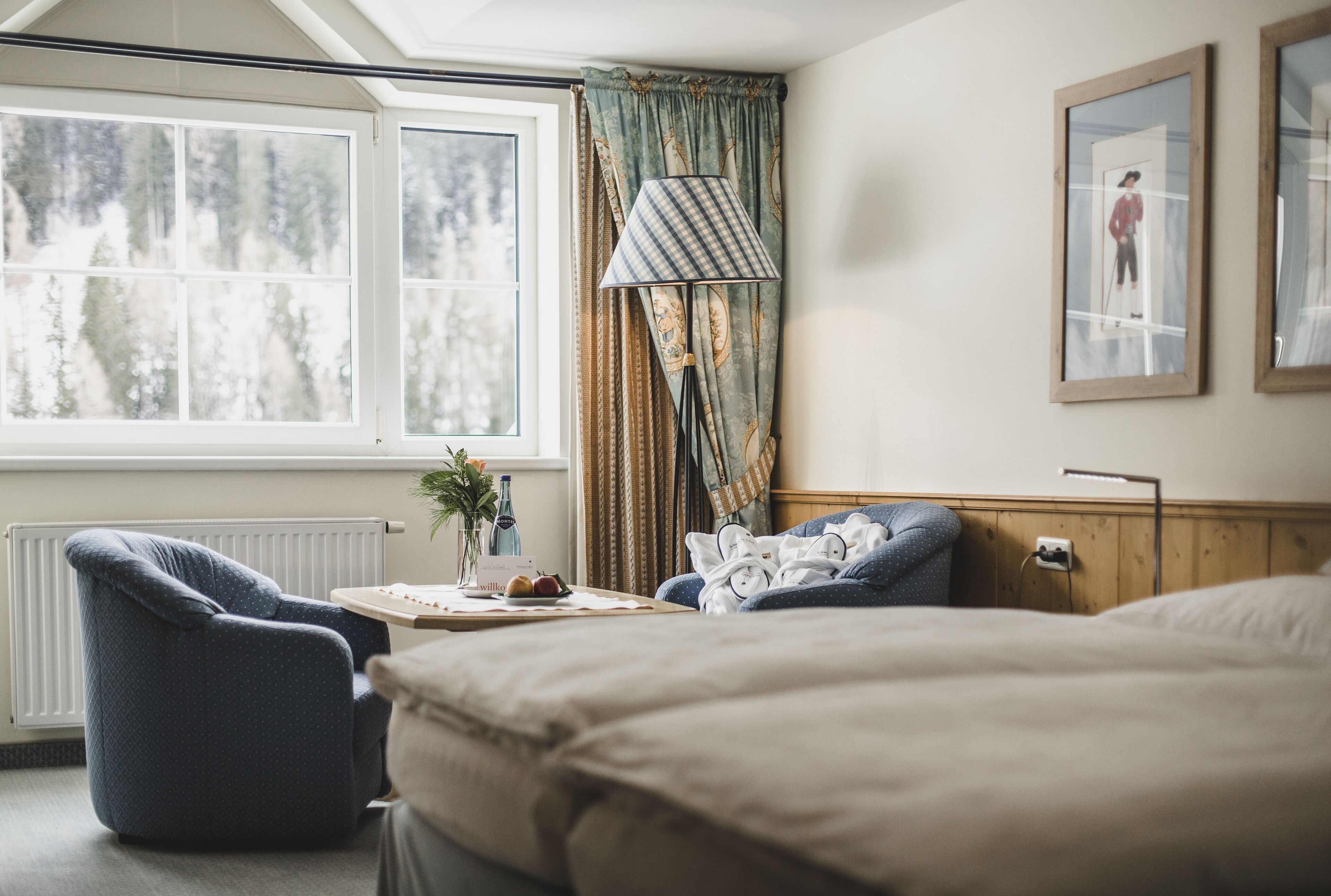 Un dormitorio con un ventanal grande, una lámpara, una silla y una cama.