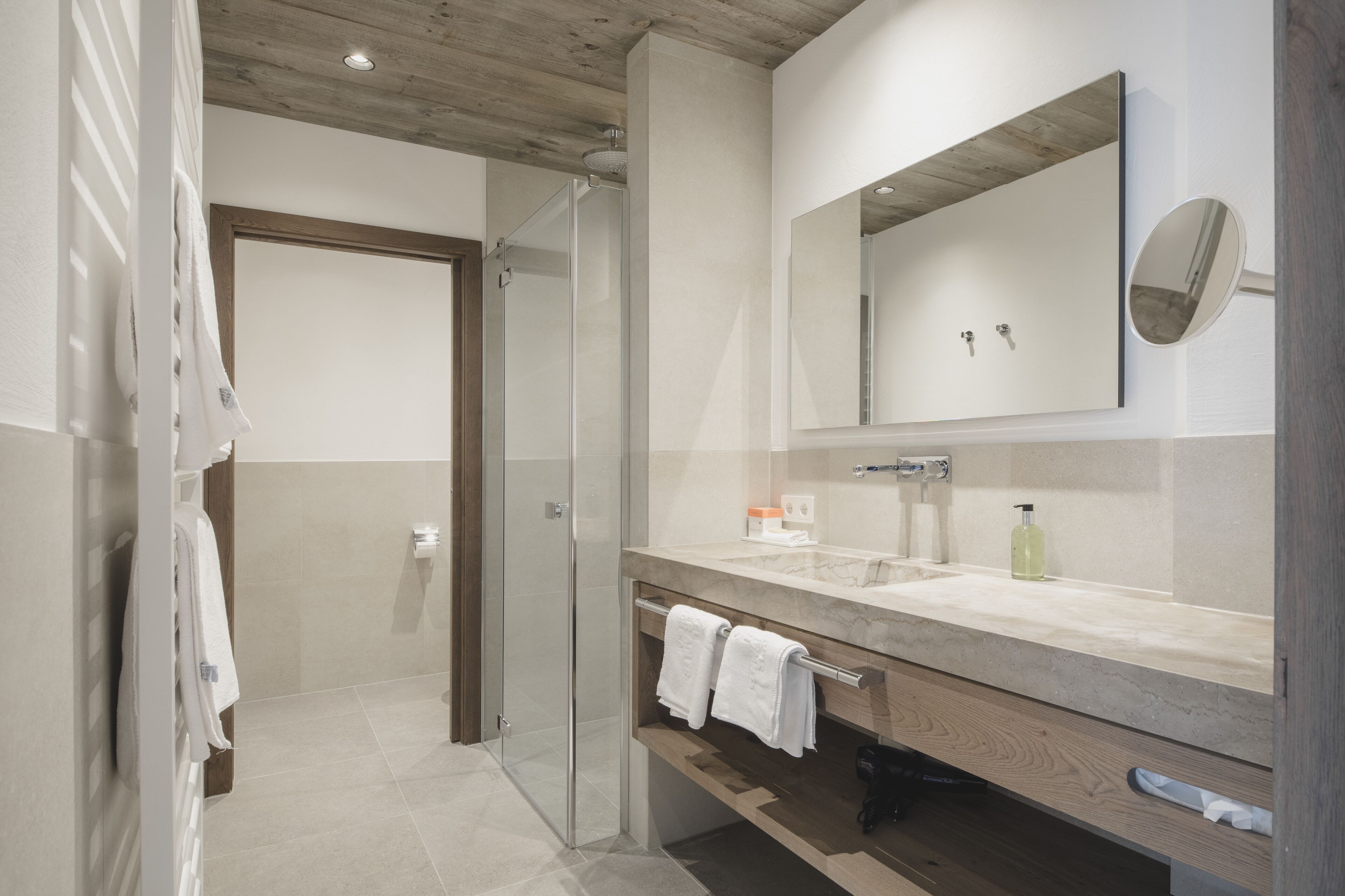 A modern bathroom with a glass shower enclosure, a large mirror, and a wooden vanity.