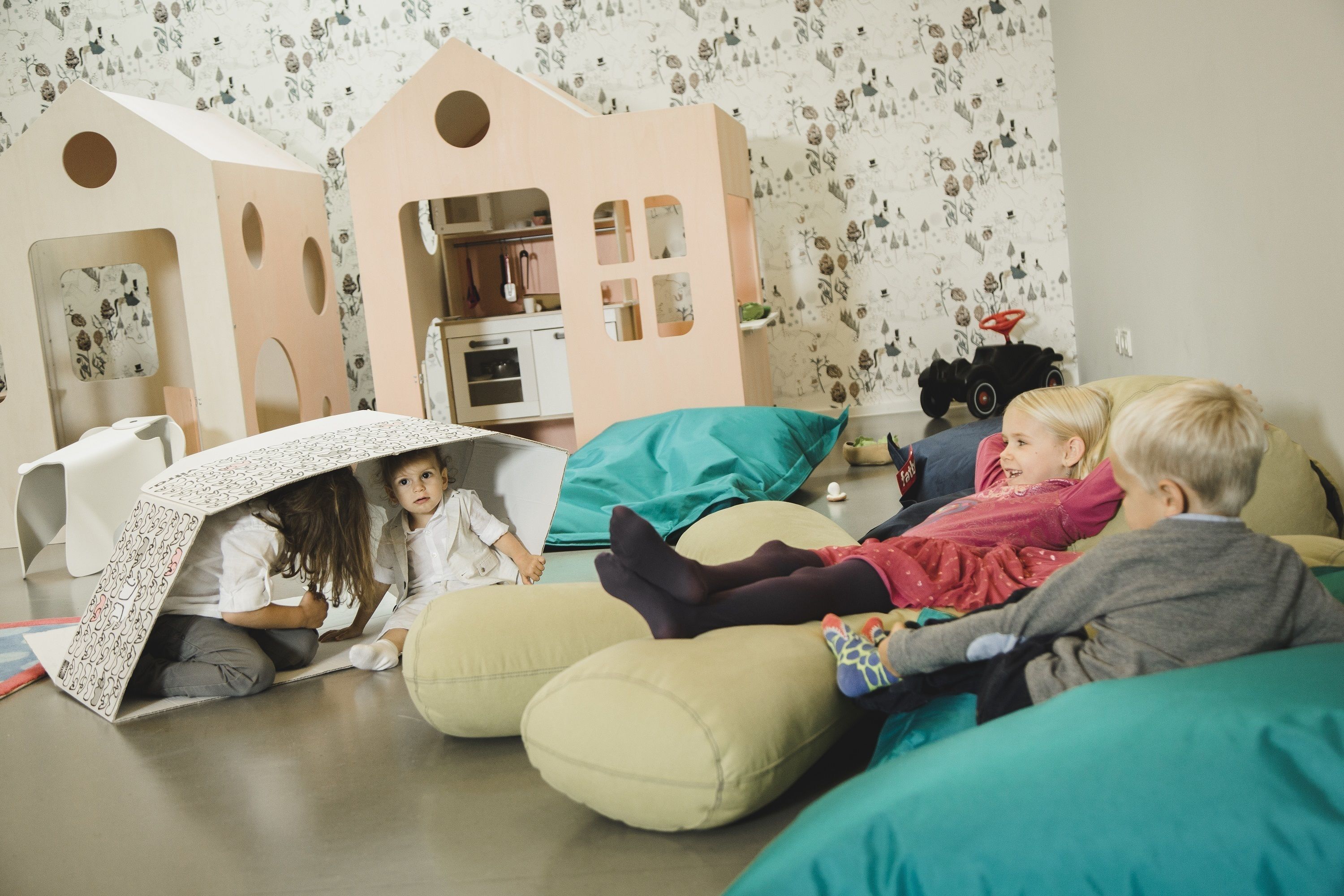 Children playing in a room with a playhouse, bean bags, and a toy car.