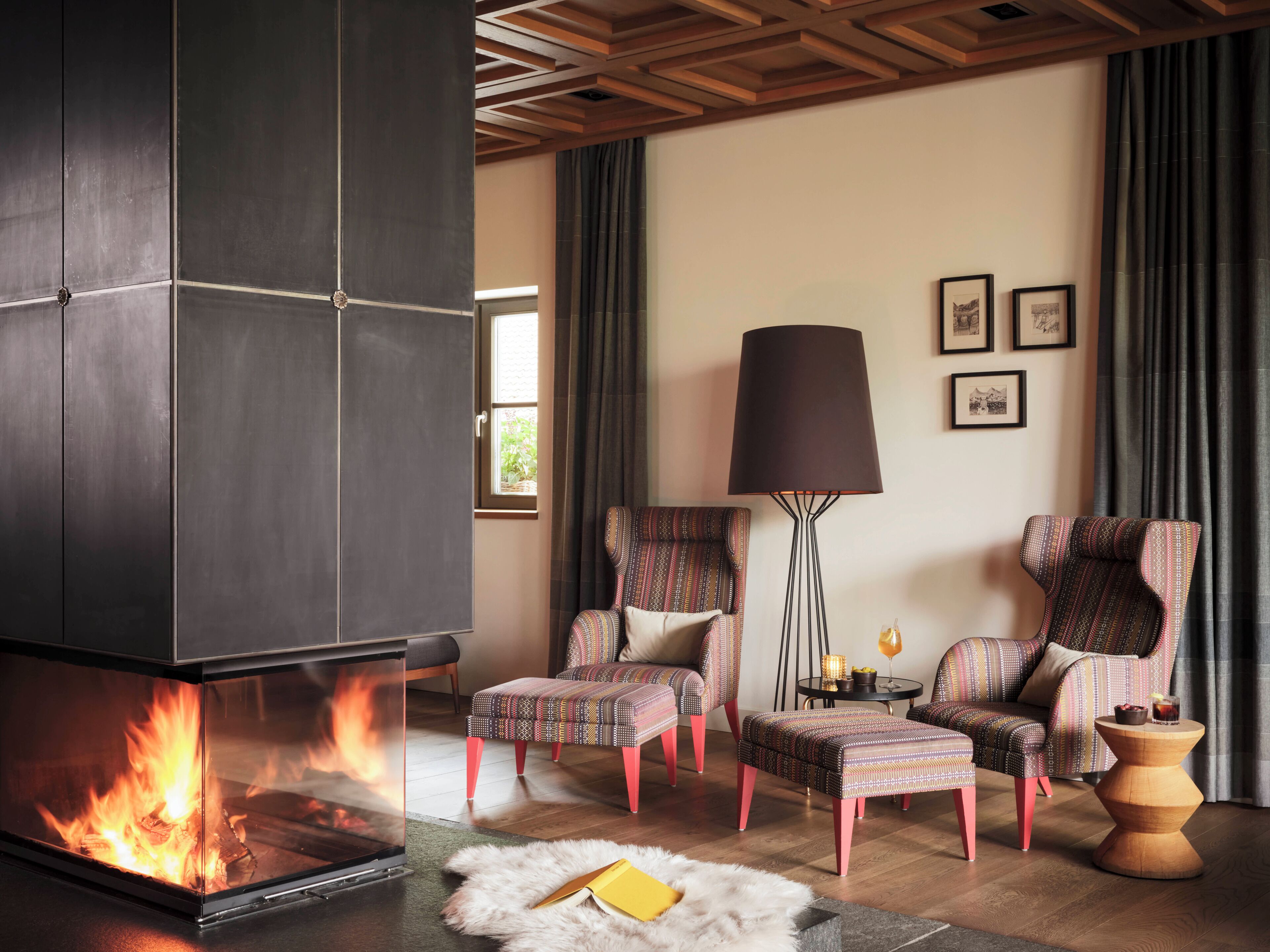 A modern living room with a fireplace, patterned armchairs, a floor lamp, and a small side table.