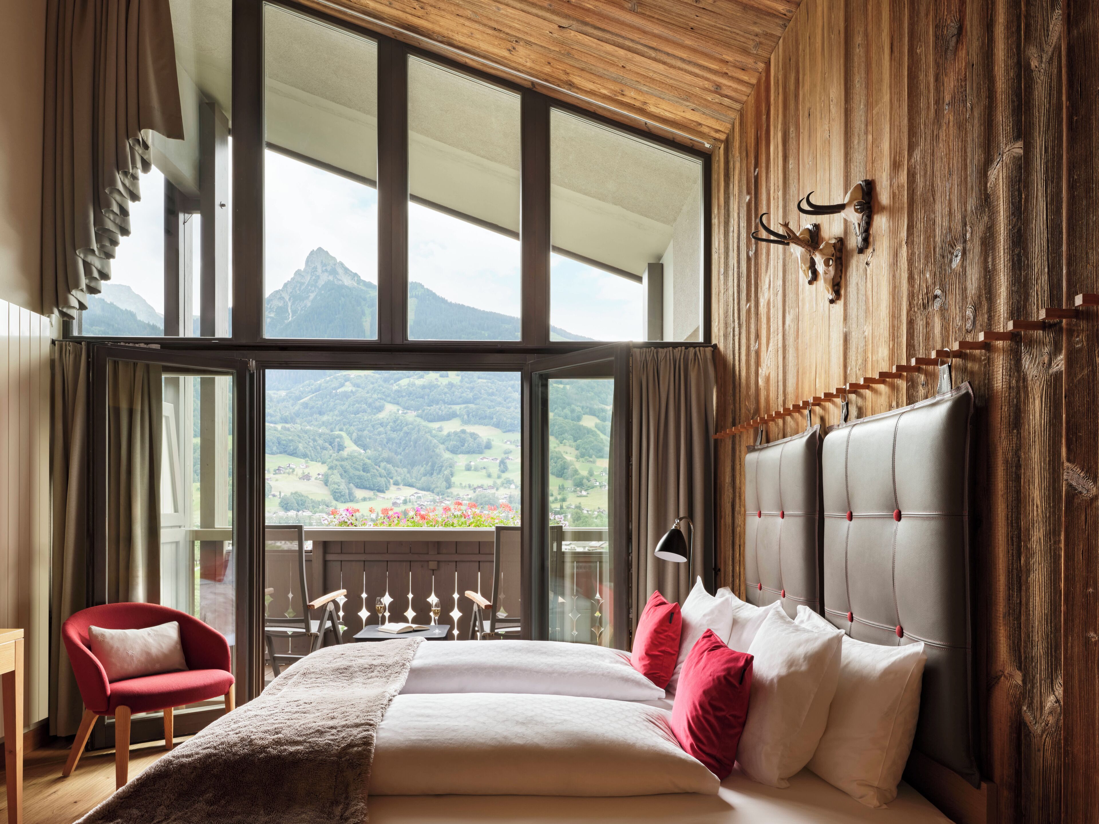 Un dormitorio con una cama grande, una silla roja y vistas a las montañas a través de amplias ventanas.