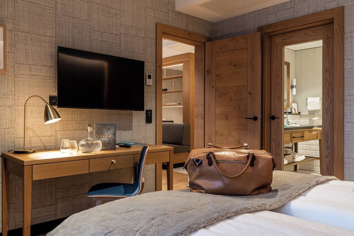 A hotel room with a wooden desk, a flat-screen TV, a bed, and a large mirror.