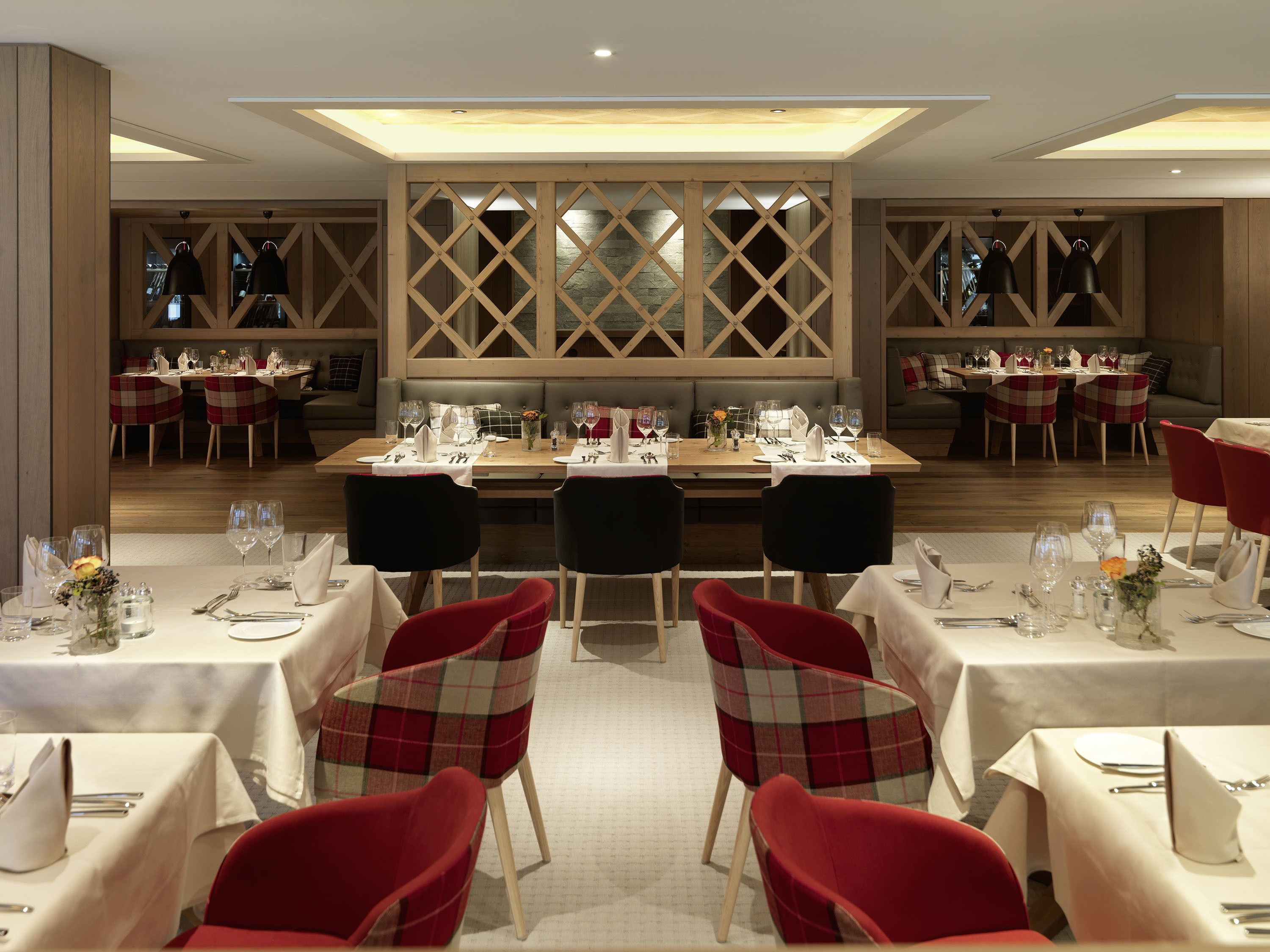 Een restaurant met een centrale eetruimte, met een lange tafel gedekt voor een maaltijd, omringd door rode fauteuils.