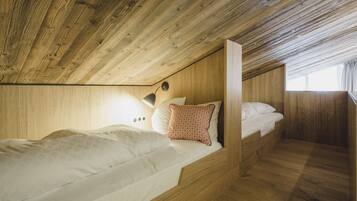 A wooden cabin bedroom with a bunk bed, a small desk, and a window with curtains.