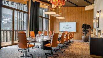 A conference room with a long table, multiple chairs, a projector screen, and a view of mountains through large windows.