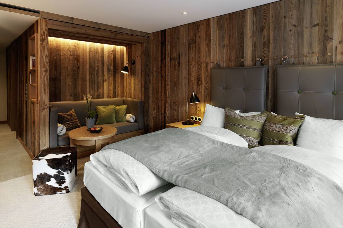 A bedroom with a wooden wall panel, a sofa, a bed with multiple pillows, and a small round table with a bowl.