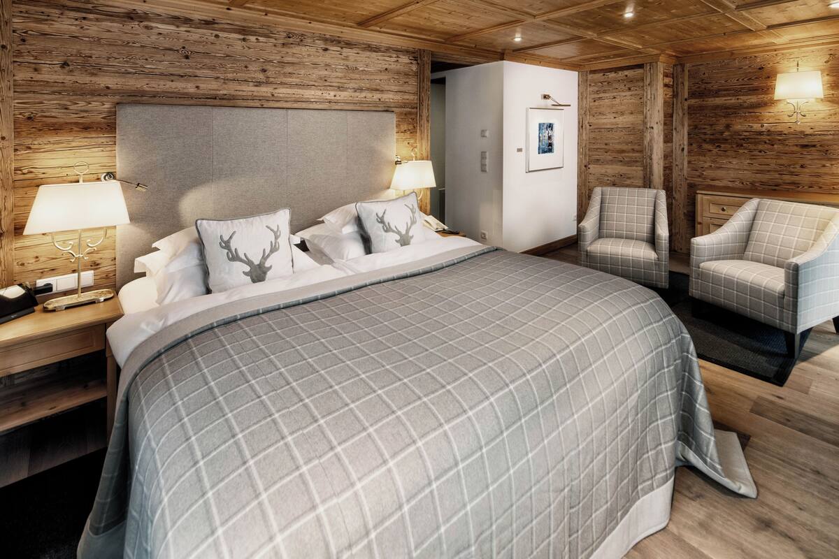 A bedroom with a large bed, two bedside tables with lamps, a wardrobe, and two armchairs.