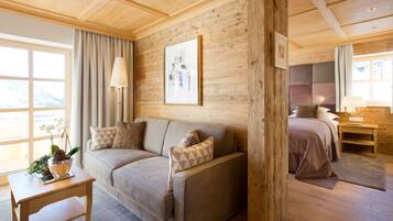 A cozy room with a wooden ceiling, a sofa with patterned cushions, a bedside table with a lamp, and a bed with a headboard.