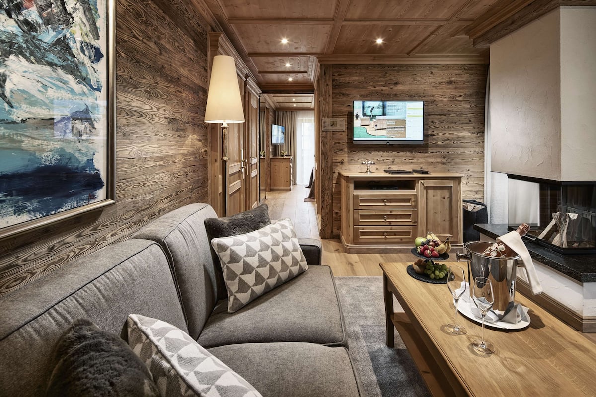 A cozy living room with a sofa, a coffee table with wine glasses, a fruit bowl, and a fireplace.