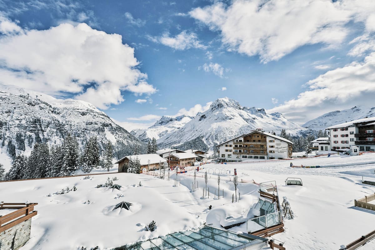 A snow-covered mountain village with chalet-style buildings, ski slopes, and a clear blue sky.
