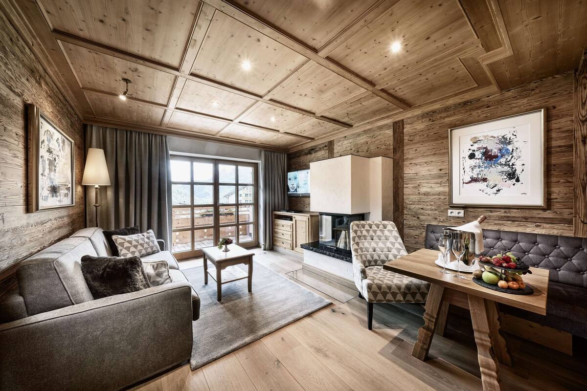 A cozy living room with a fireplace, a sofa, a dining table with fruit, and a large window.