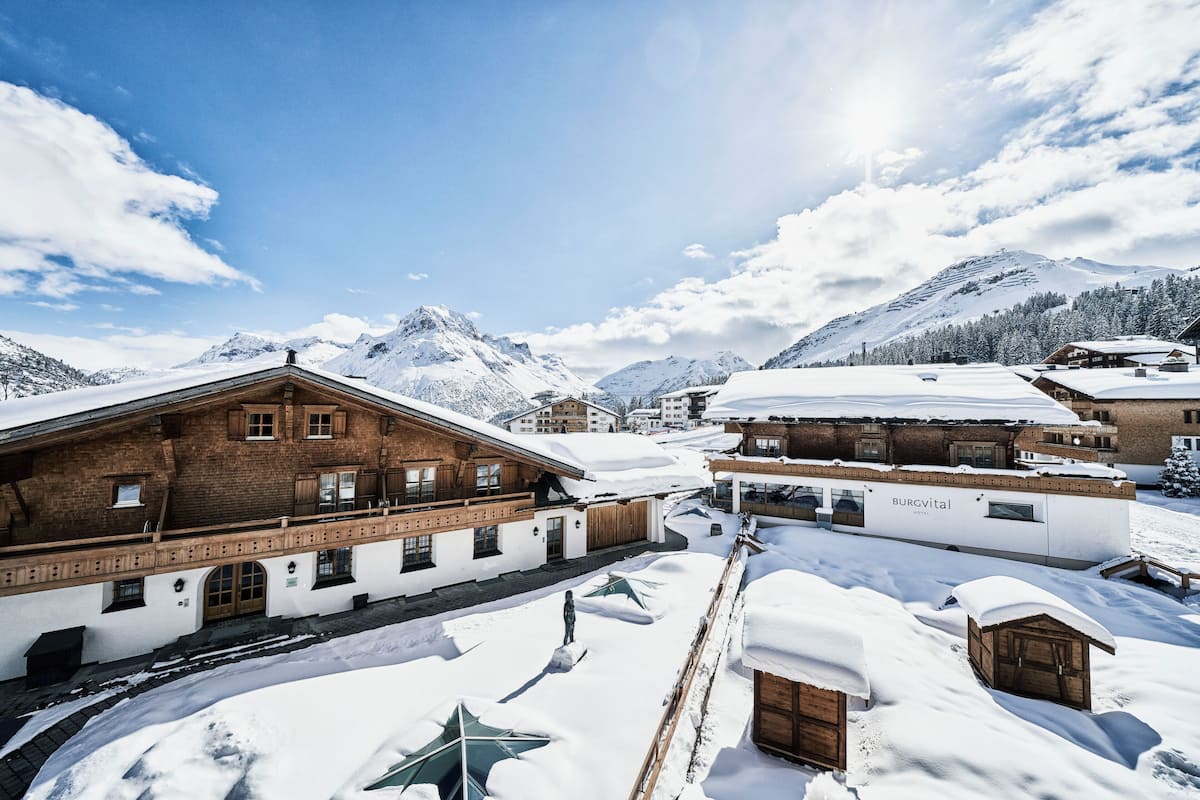 A snow-covered village with traditional wooden buildings, including a hotel named BURGvital.