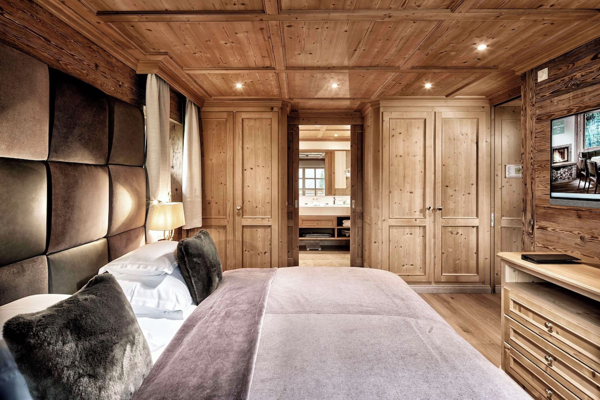 A wooden-paneled bedroom with a bed, a TV, and a view of a dining area.