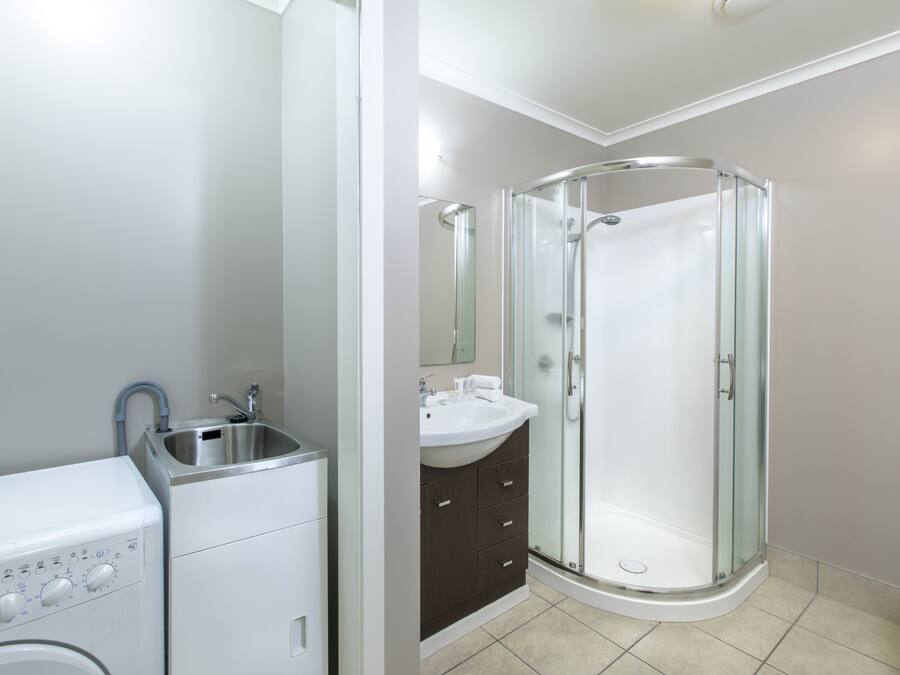 Un baño moderno con ducha de vidrio, lavamanos integrado y lavadora.