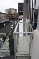 A high-rise building with a glass balcony overlooking a street with parked cars and a pedestrian.