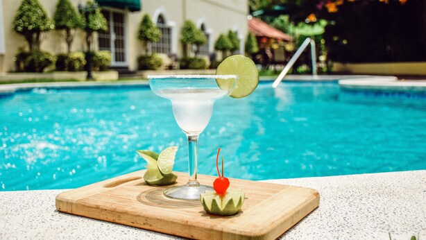 A margarita on a wooden tray by a pool with a building in the background. - Hotel Mirador Plaza (San Salvador)