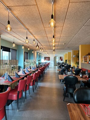 Un restaurant spacieux avec de longues tables et des chaises rouges, un éclairage suspendu et un aménagement intérieur moderne.