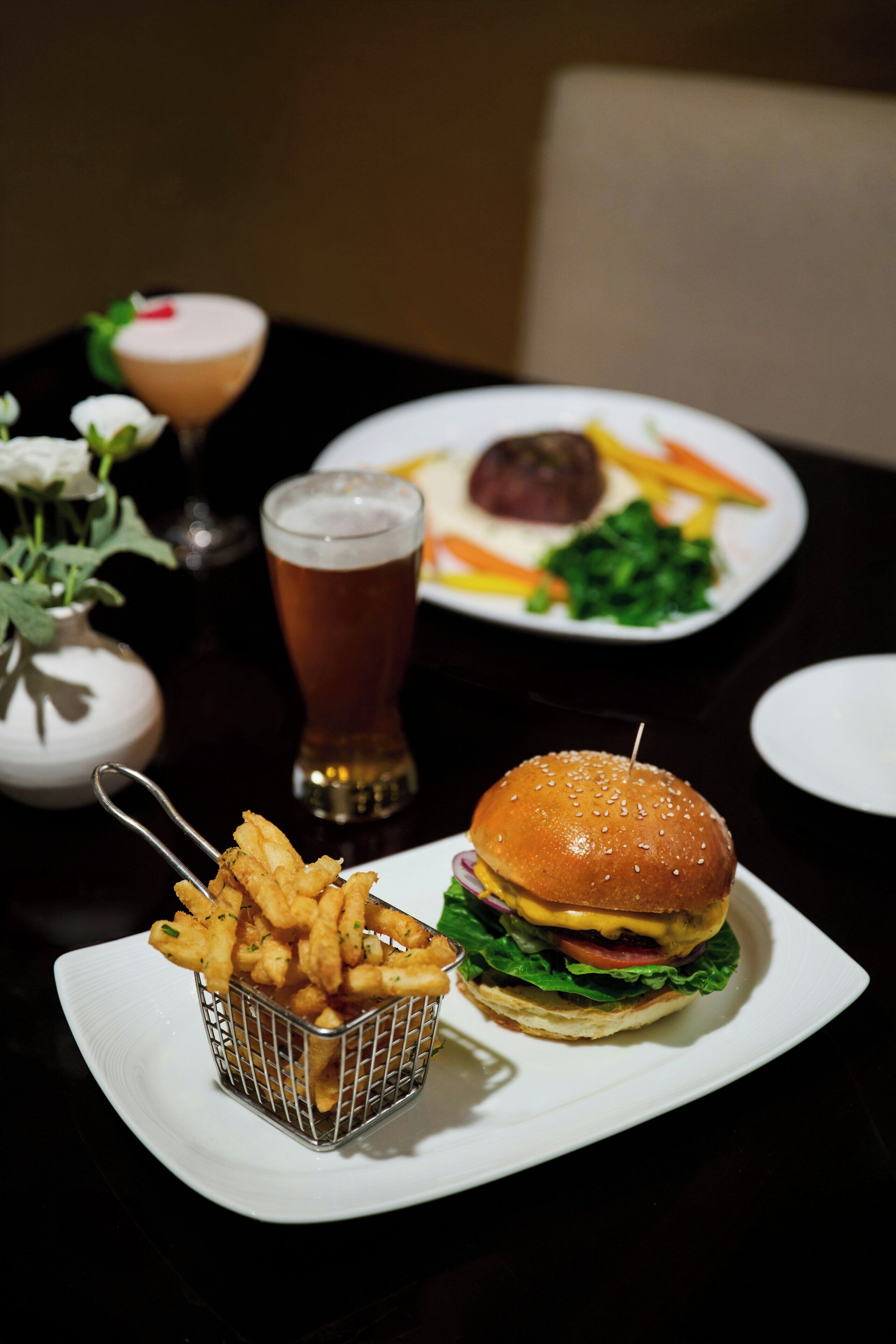A dining table with a burger, fries, and a beer.