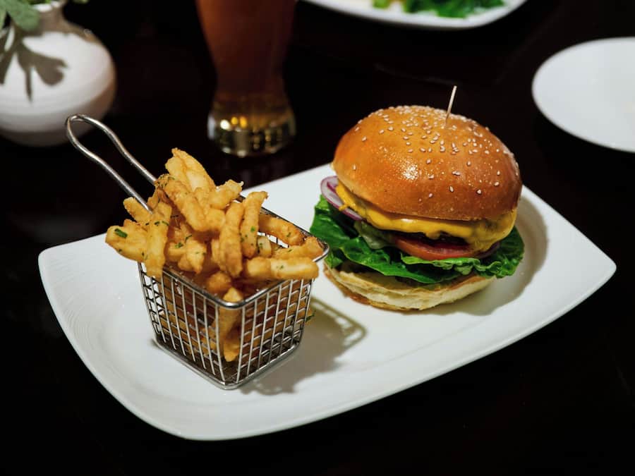 A dining table with a burger, fries, and a beer.
