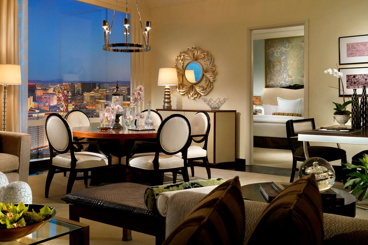 Une chambre d’hôtel moderne avec vue sur la ville, un coin repas agrémenté d’un lustre, et un espace salon confortable offrant une vue panoramique sur le paysage urbain.
