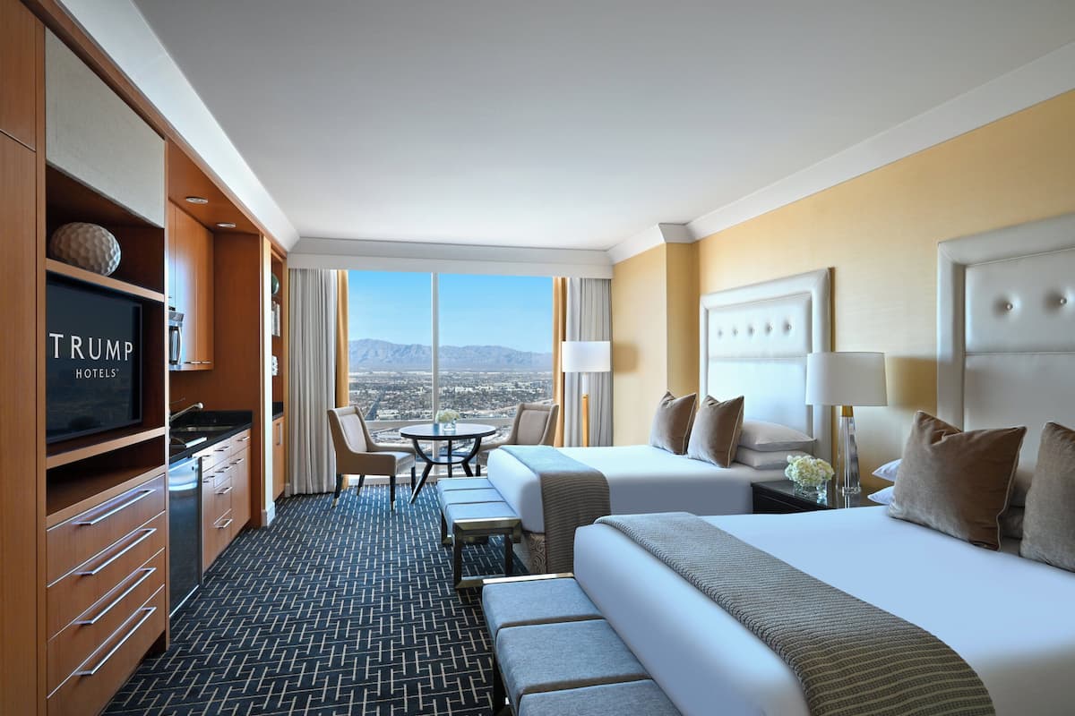 Une chambre d’hôtel équipée d’une télévision diffusant le logo « TRUMP HOTELS », d’un lit, d’un bureau, d’une chaise et offrant une vue sur les montagnes.