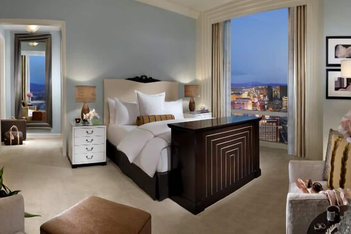 Une chambre d’hôtel avec un grand lit, un bureau, une table de chevet, une commode et une vue sur le paysage urbain.