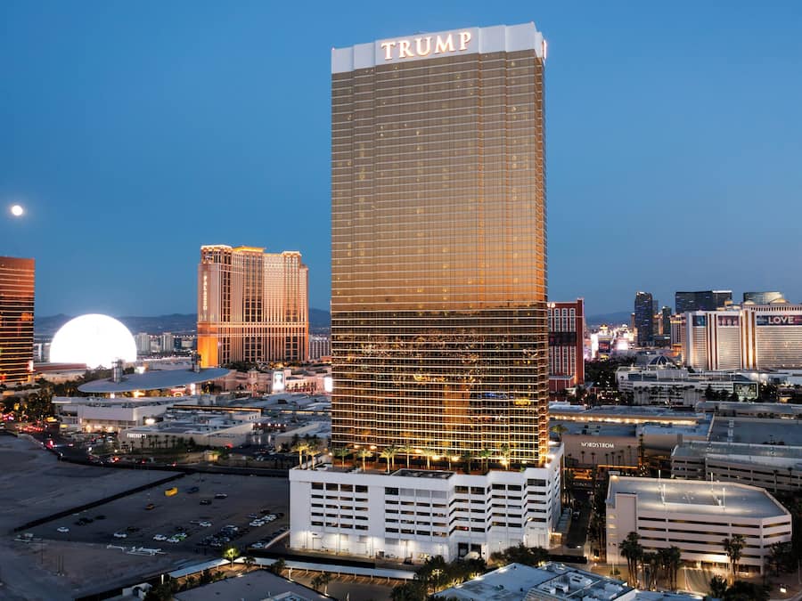 A high-rise hotel with a prominent 'TRUMP' sign, surrounded by other buildings and a parking area.