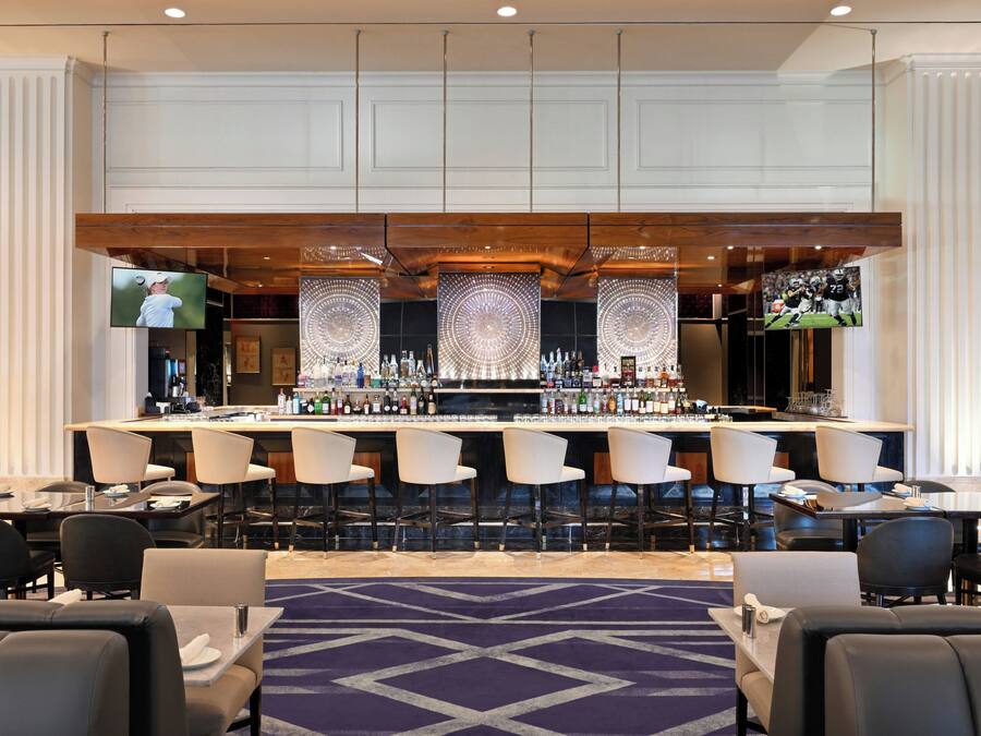 A bar area with multiple seating options, a variety of bottles, and a television screen.