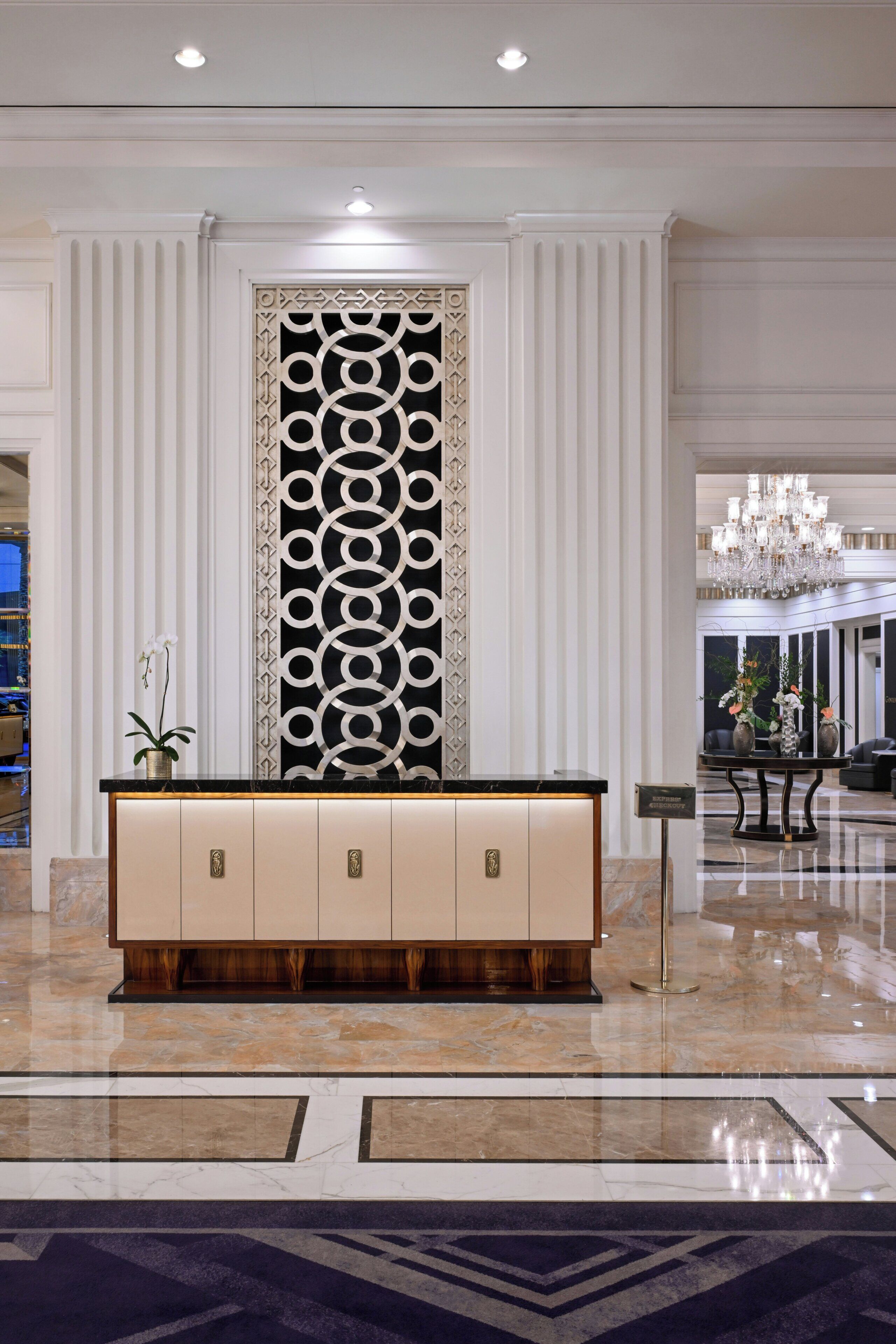 A lobby with a reception desk, a decorative wall, and a chandelier.
