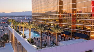 A hotel with a rooftop pool surrounded by palm trees, a view of the cityscape, and a mountain range in the background.