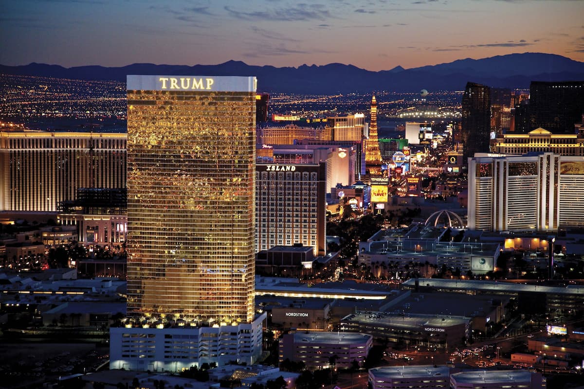 Un grand hôtel, avec le nom « TRUMP » écrit en grandes lettres sur sa façade, qui se dresse au milieu d’autres immeubles et des lumières de la ville.