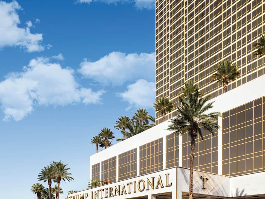 A Trump International hotel with a modern facade, palm trees, and a clear sky.