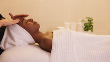 Eine Person liegt auf einem Bett mit einem weißen Handtuch, eine Hand ruht auf dem Kopf, und im Hintergrund steht eine Pflanze.