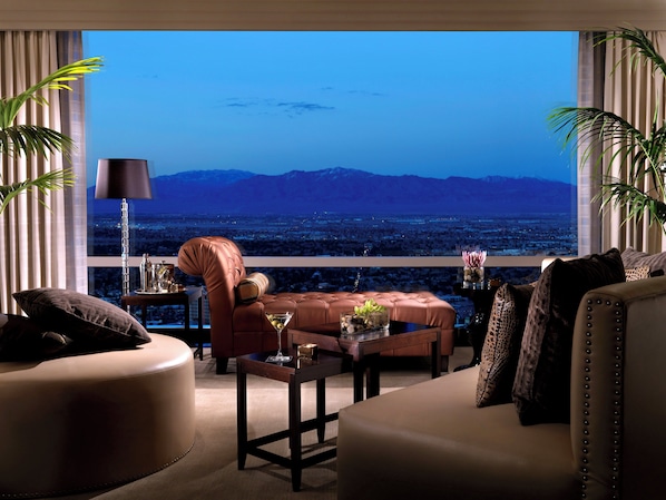 A modern living room with a leather sofa, a coffee table, and a view of a cityscape at dusk.