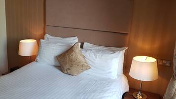Una cama bien tendida con sábanas blancas y dos almohadones decorativos, con dos lámparas de noche a cada lado.